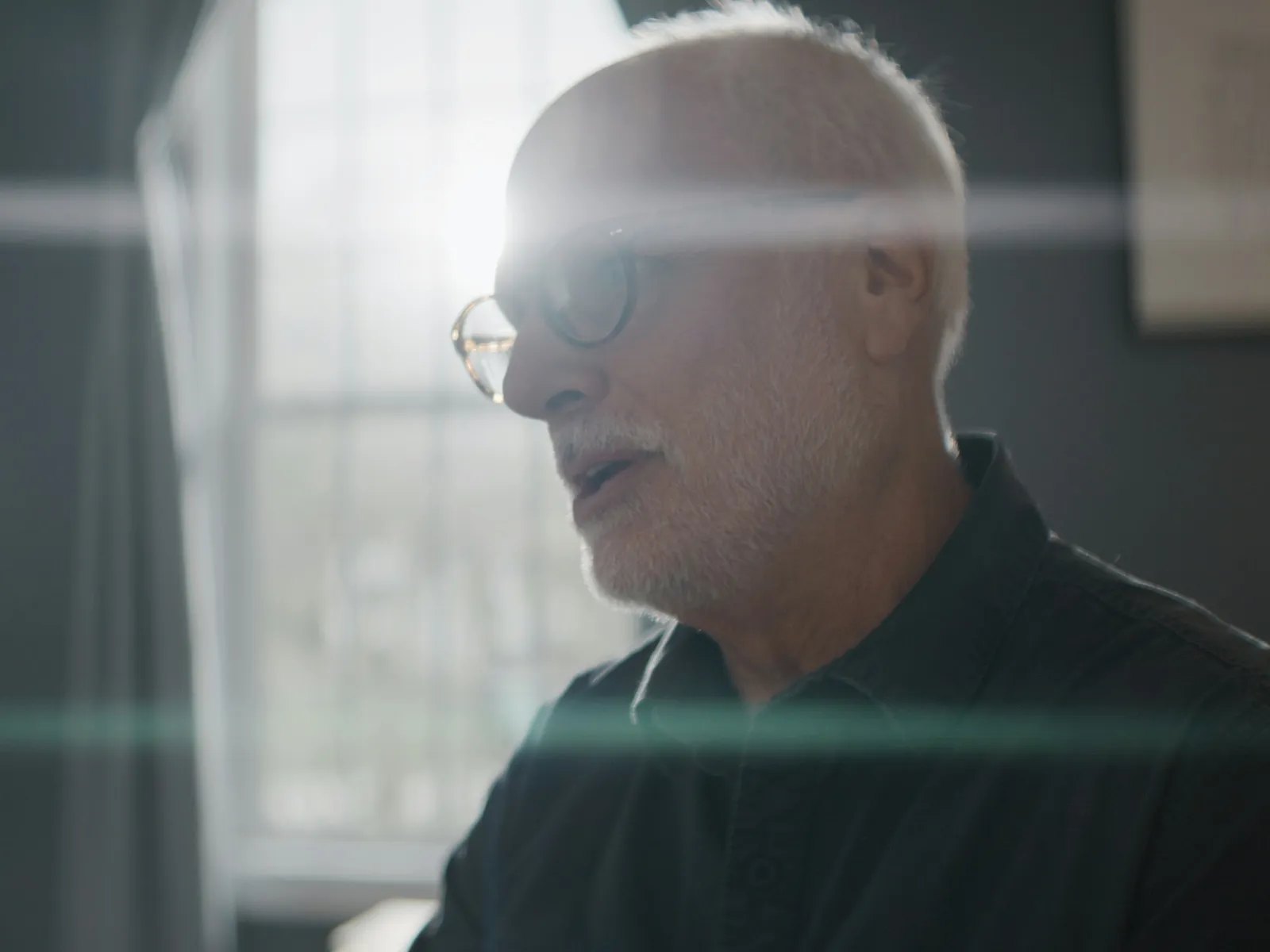 An older man sitting quietly by a window in low evening light at home
