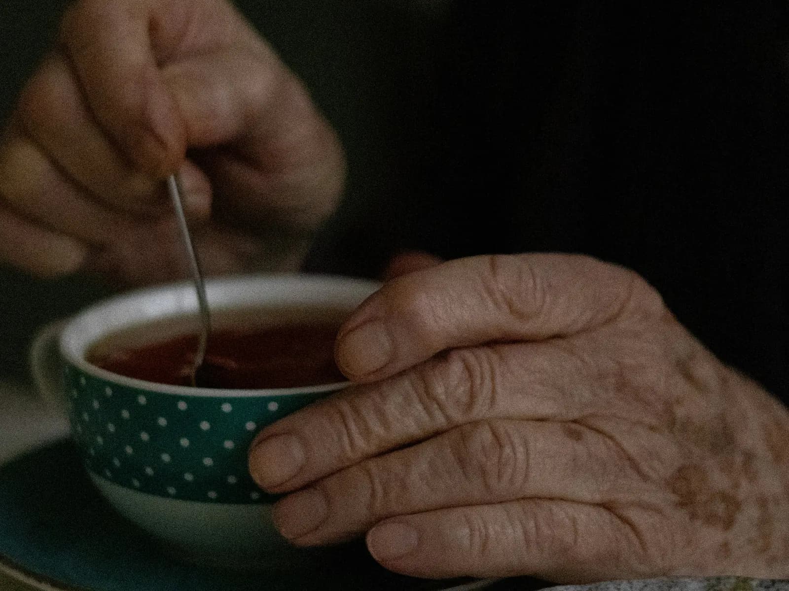 An older person's hands resting quietly around a mug of tea